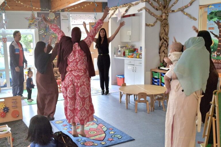 Children playing under a rainbow parachute with live guitar music at Little Fingers under 5s play group
